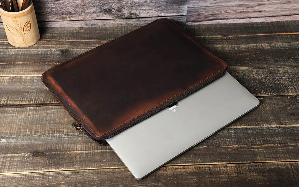 Brown leather laptop sleeve on a silver laptop on a wooden surface