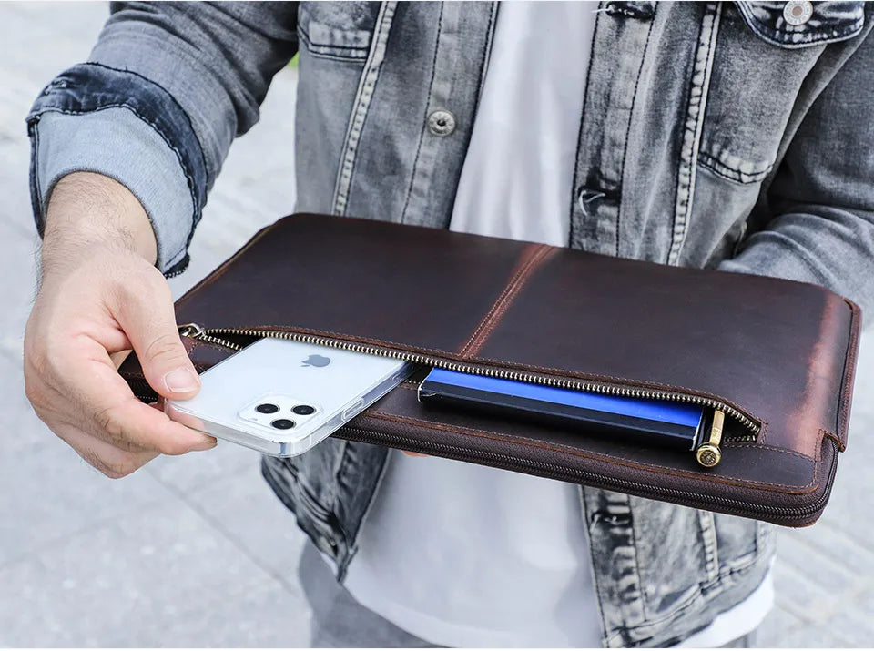 Person holding a brown leather wallet with a phone and another device inside, wearing a denim jacket.