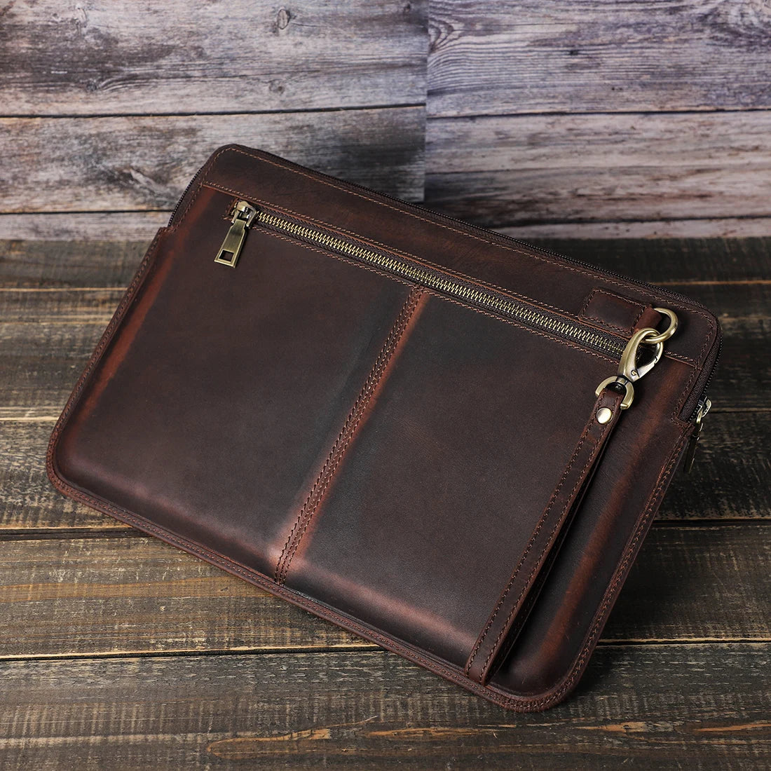 Brown leather clutch bag with gold zipper on a wooden surface