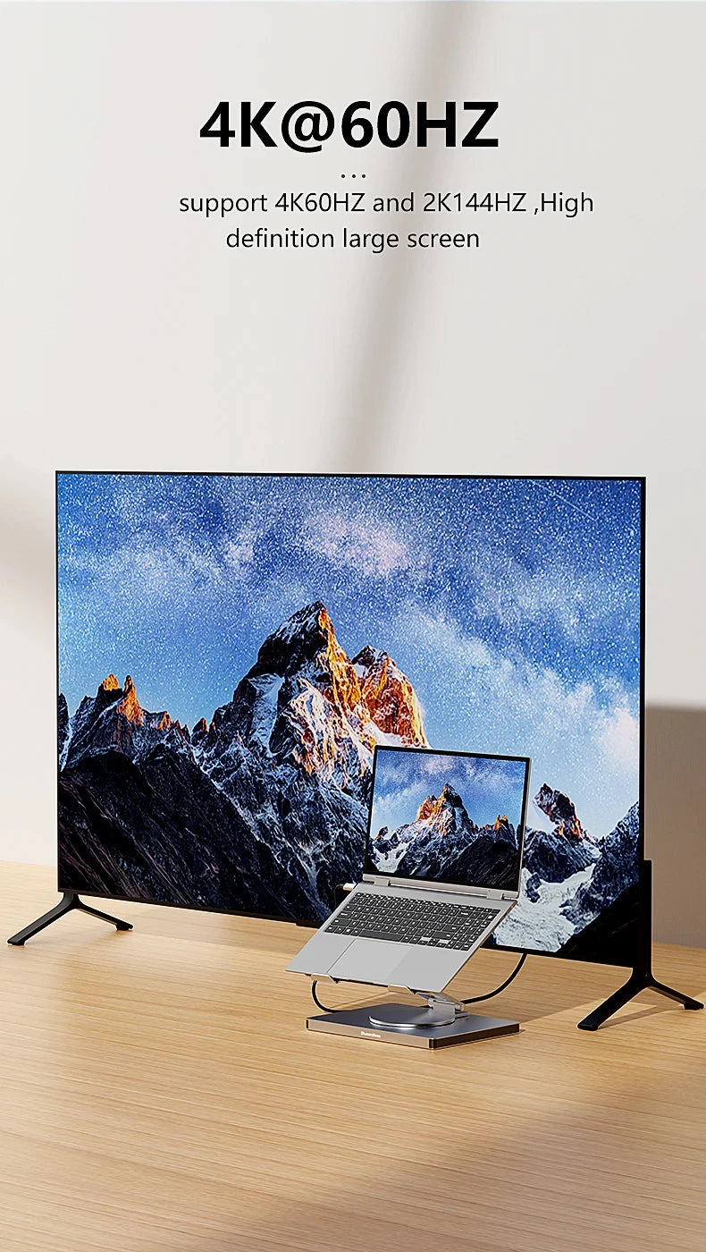 Large screen displaying a mountain scene with a laptop on a stand below, on a wooden surface.